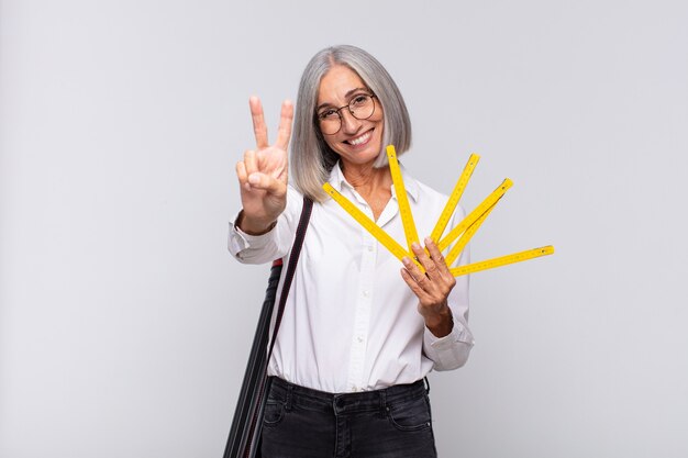 Mulher de meia-idade sorrindo e parecendo feliz, despreocupada e positiva, gesticulando vitória ou paz com uma mão. conceito de arquiteto