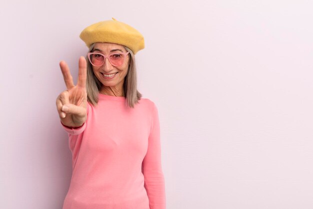 Mulher de meia idade sorrindo e parecendo feliz gesticulando vitória ou paz