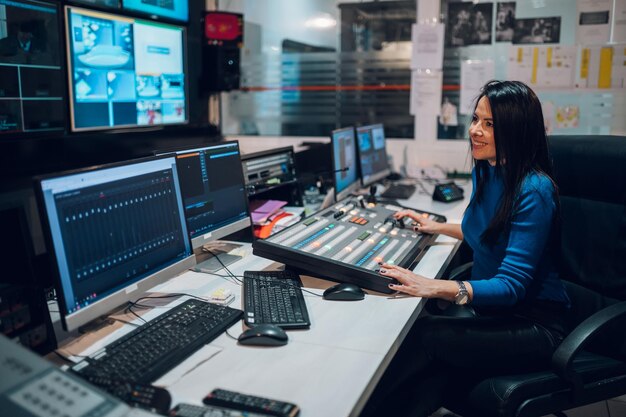 Mulher de meia idade usando equipamento na sala de controle em uma estação de tv