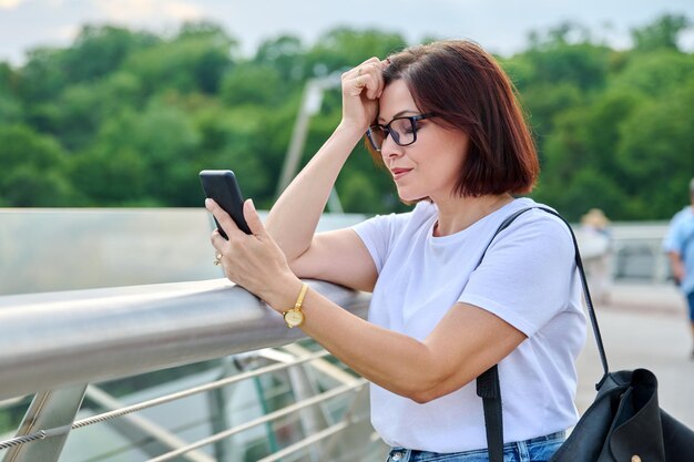 Mulher de meia idade usando smartphone andando na cidade de verão