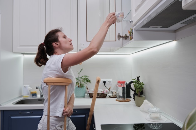 Mulher de muletas lava a louça na cozinha
