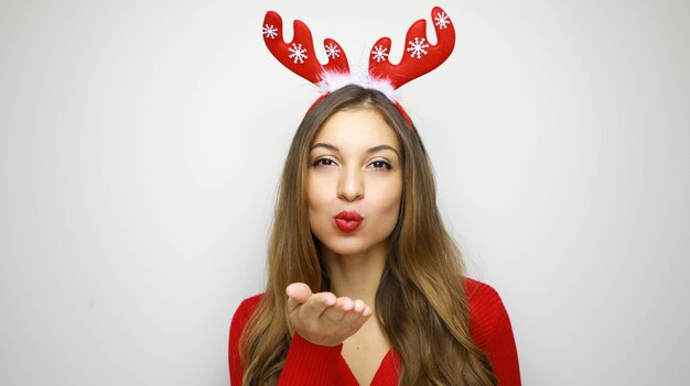 Mulher de Natal com lábios vermelhos soprando manda beijo no ar com chifres de rena na cabeça