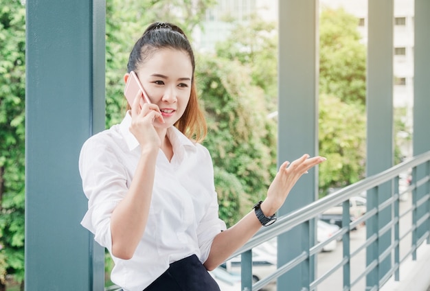 Mulher de negócio asiática com camisa branca falando no telefone inteligente para o trabalho