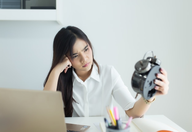 Mulher de negócio asiática nova que olha o despertador em seu local de trabalho.