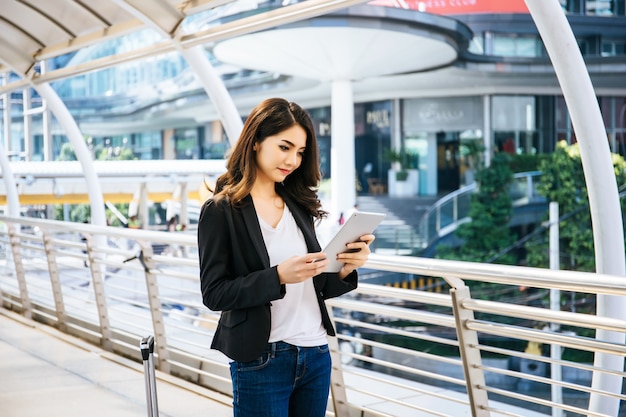Mulher de negócio atraente que usa um comprimido digital enquanto está em frente ao prédio de escritórios.