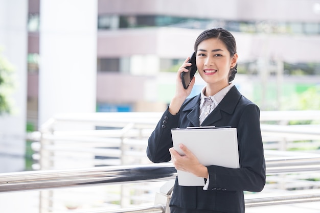 Mulher de negócio bonita nova na cidade usando o smartphone para o trabalho.