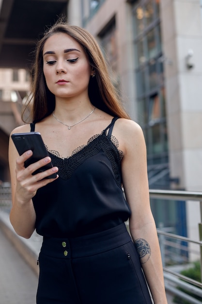 Mulher De Negócio Com O Telefone Perto Do Escritório. Retrato da bela mulher sorridente em roupas de escritório da moda, falando no telefone enquanto em pé ao ar livre. Comunicação por telefone. Imagem de alta qualidade.