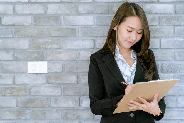 Mulher de negócio nova bonita asiática na saia do terno usando o documento de trabalho sobre vendas e plano de marketing