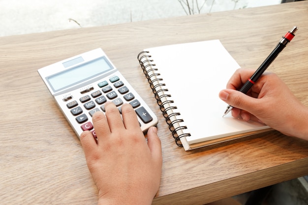 Mulher de negócio que empurra a calculadora com caderno e pena na mesa - conceito de trabalho.