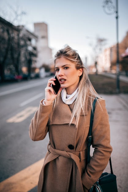 Mulher de negócios à moda que usa o telefone esperto ao esperar um táxi.