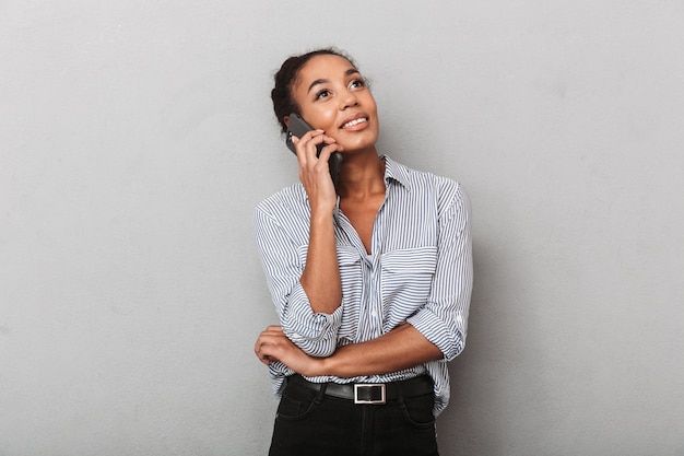 Mulher de negócios africana confiante vestindo uma camisa isolada sobre o cinza, falando no celular