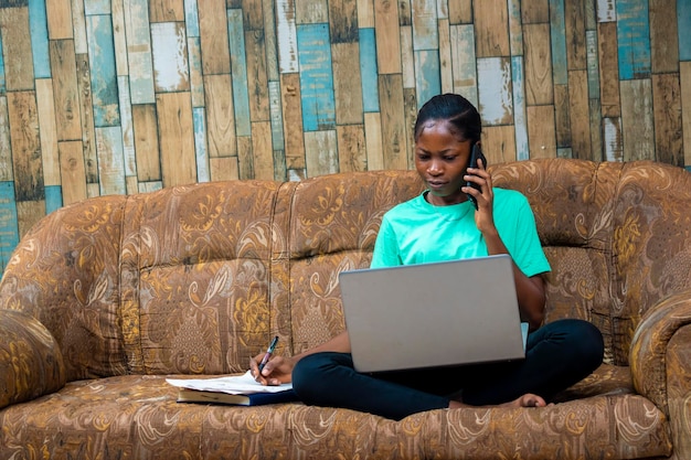 Mulher de negócios africana jovem fazendo telefonema usando o computador portátil