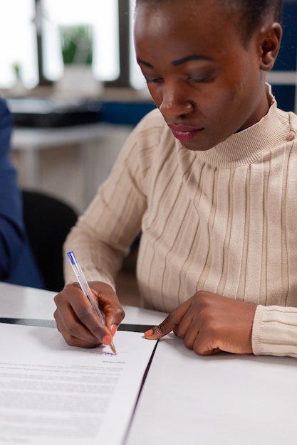 Mulher de negócios africana lendo documentos de assinatura, enquanto parceiros de negócios compartilham papelada