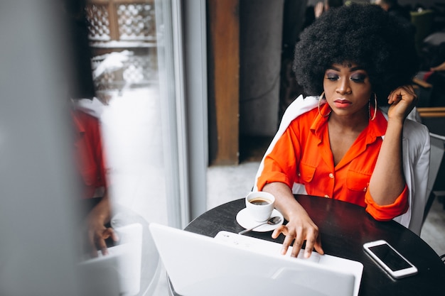 Mulher de negócios afro-americana em terno branco trabalhando no laptop em um café