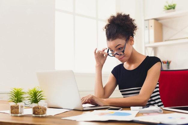 Mulher de negócios afro-americana feliz trabalhando no laptop no escritório. Empresária digitando algo no computador enquanto está sentada no local de trabalho, copie o espaço