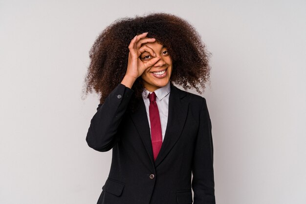 Mulher de negócios afro-americana jovem vestindo um terno isolado no branco animado, mantendo o gesto ok no olho.