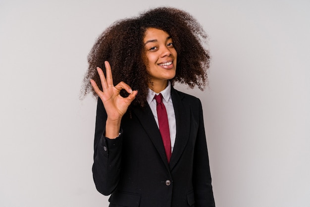 Mulher de negócios afro-americana jovem vestindo um terno isolado no fundo branco, alegre e confiante, mostrando um gesto ok.