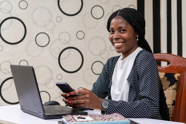 Mulher de negócios afro-americana sorrindo enquanto opera o telefone no escritório