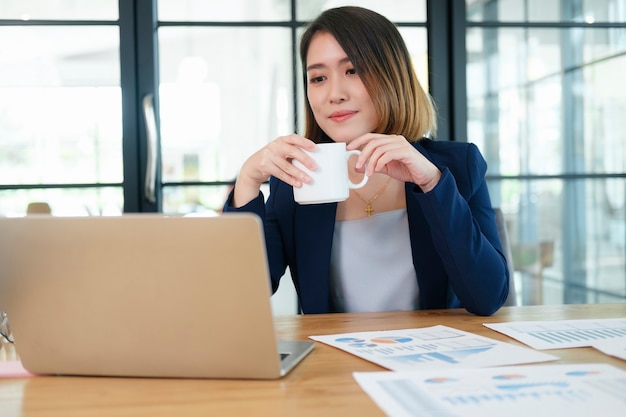 Mulher de negócios alegre segurando a xícara de café no escritório e olhando para a câmera.