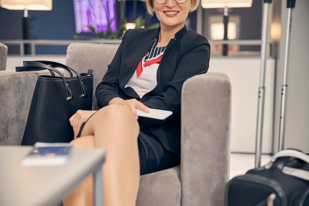 Mulher de negócios alegre segurando um smartphone e sorrindo enquanto espera seu voo no corredor