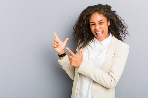 Mulher de negócios americano africano jovem apontando com o dedo indicador para um espaço de cópia, expressando emoção e desejo.