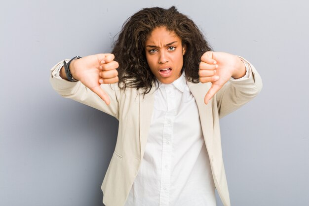 Mulher de negócios americano africano jovem mostrando o polegar para baixo e expressando antipatia.