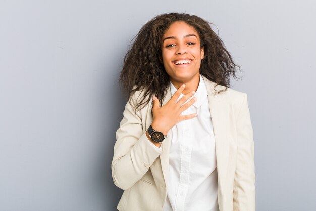 Mulher de negócios americano africano jovem ri alto, mantendo a mão no peito.