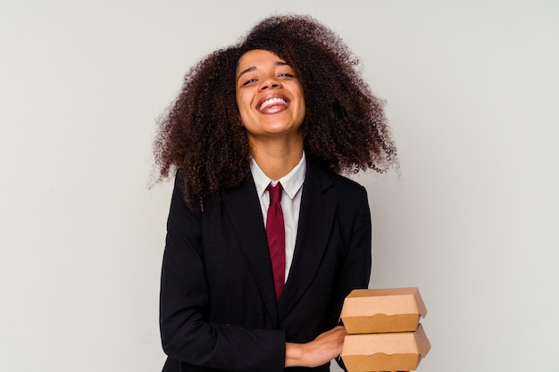 Mulher de negócios americano africano jovem segurando um hambúrguer isolado no fundo branco, rindo e se divertindo.