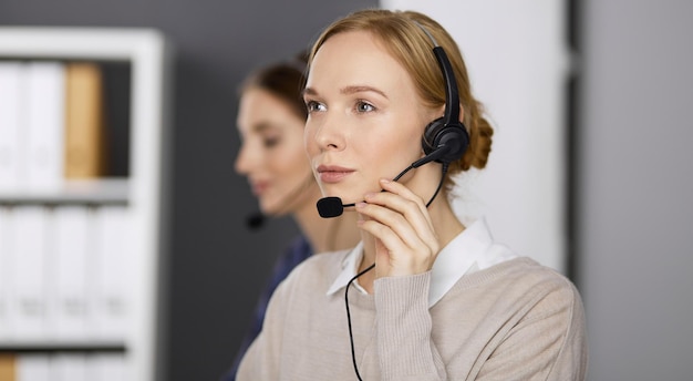 Mulher de negócios amigável a falar por fone de ouvido enquanto está sentada no escritório.