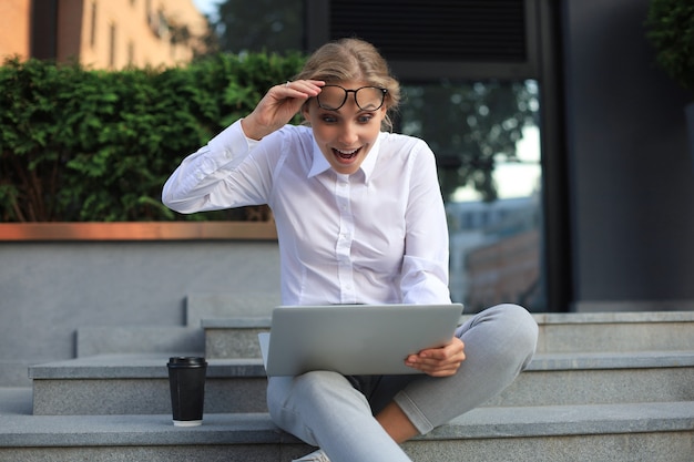 Mulher de negócios animado bonita sentado perto do centro de negócios e usando o laptop.