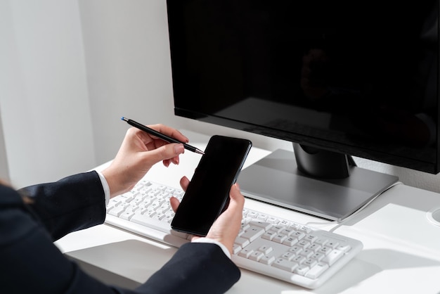 Mulher de negócios apontando com caneta no celular com mensagem importante sentado na mesa com computador Mulher de terno tendo celular com informações cruciais