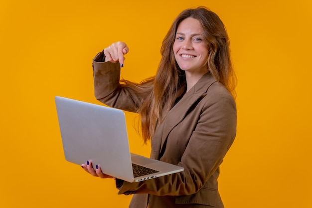 Mulher de negócios apontando para um computador em um conceito de jovem empreendedor de fundo amarelo