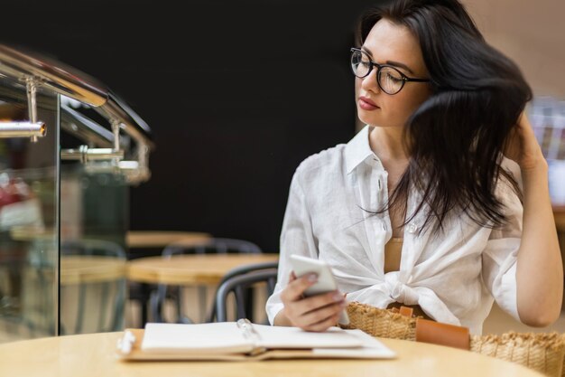Mulher de negócios asiática agradável conversando usando smartphone fazendo anotações no bloco de notas à mesa no café