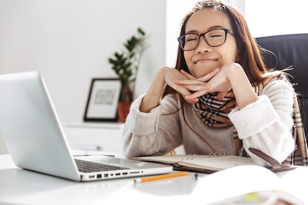 Mulher de negócios asiática alegre descansando de olhos fechados enquanto está sentada à mesa no escritório