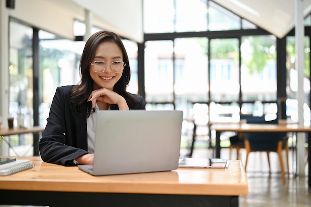 Mulher de negócios asiática atraente pensando em uma estratégia de negócios para nova campanha usando laptop