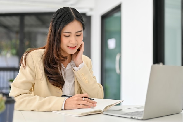 Mulher de negócios asiática com foco em suas tarefas fazendo anotações em seu notebook trabalhando em sua mesa