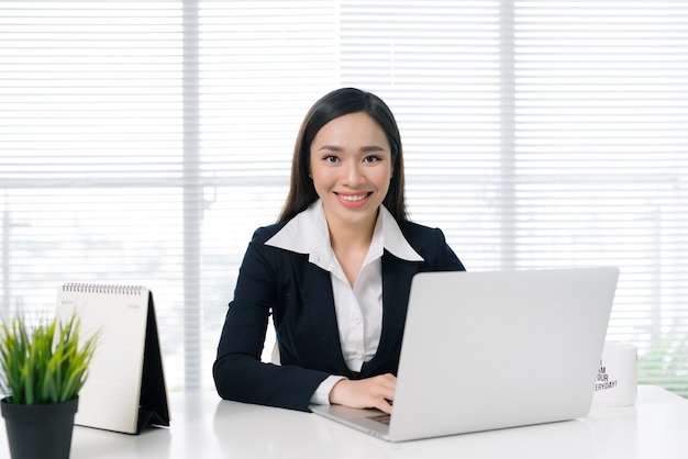 Mulher de negócios asiática confiante sentada à mesa com o laptop no escritório