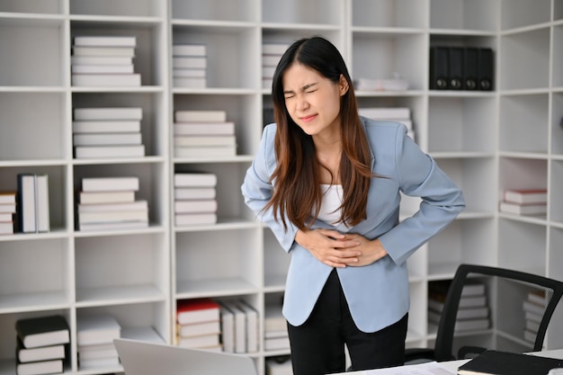 Mulher de negócios asiática doente que sofre de dor de estômago ou dor abdominal em seu escritório