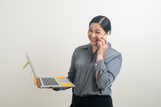 Mulher de negócios asiática falando ao telefone com a mão segurando um laptop no fundo branco