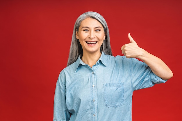 Mulher de negócios asiática idosa madura elegante feliz sorrindo em pé isolado sobre fundo vermelho sorrindo confiante e alegre senhora de meia idade cópia espaço polegares para cima sinal