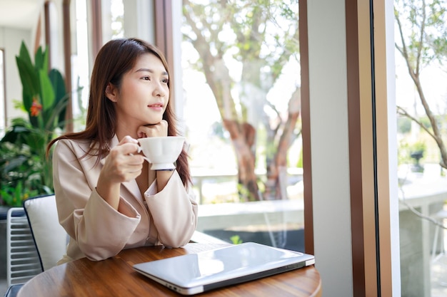 Mulher de negócios asiática inteligente bebendo café e trabalhando por laptop na cafeteria