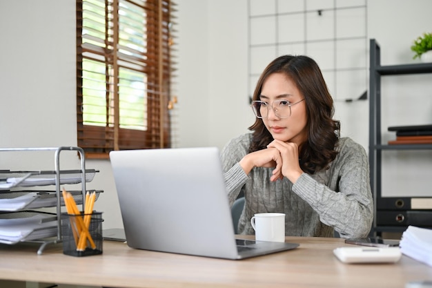 Mulher de negócios asiática inteligente concentrando-se em suas tarefas olhando para a tela do laptop