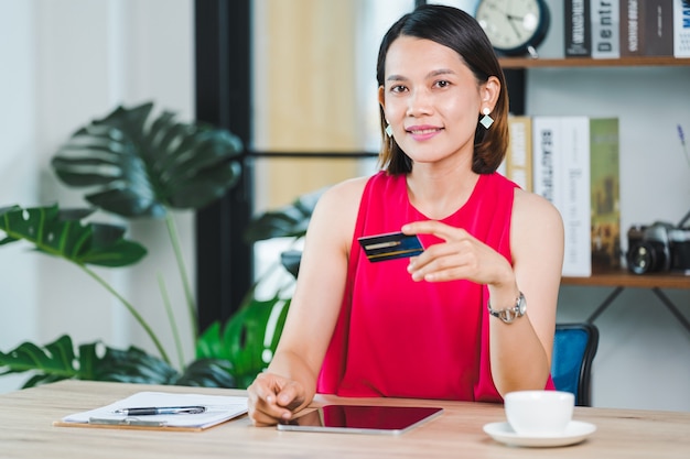 Mulher de negócios asiática segurando o cartão de crédito e usando o laptop em casa. Homem de negócios ou empreendedor trabalhando, compras online, e-commerce, internet banking, trabalhando em casa conceito