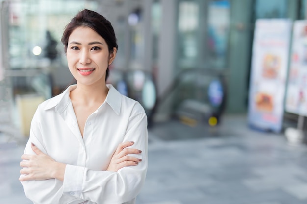 Mulher de negócios asiática sorridente desfocando o fundo do prédio de escritórios