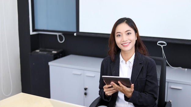 Mulher de negócios asiática sorridente usando tablet para trabalhar e garota bonita procurando alguns dados e se concentrar em seu tablet em seu escritório