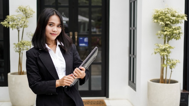 Mulher de negócios asiática sorrindo com um envelope pardo e parada na frente do escritório