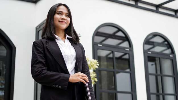 Mulher de negócios asiática sorrindo com um envelope pardo e parada na frente do escritório