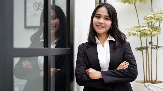 Mulher de negócios asiática sorrindo e parada na frente do escritório