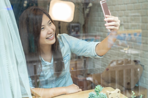 Mulher de negócios asiática tomando o selfie com ação de felicidade na cafeteria moderna