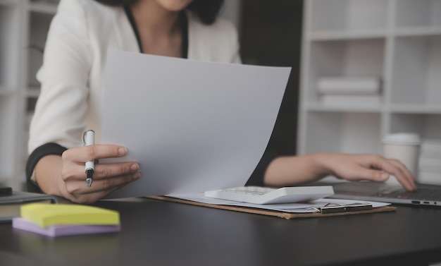 Mulher de negócios asiática Usando computador portátil e trabalhando no escritório com calculadora documento na mesa fazendo planejamento analisando o relatório financeiro plano de negócios conceito de análise de financiamento de investimento